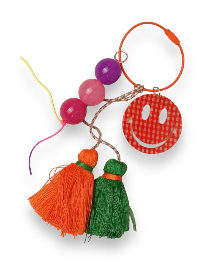 red check pattern smiley face on a large ring with pink and purple beads and orange and green tassels